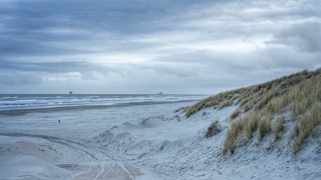 Buren beach on the Dutch island Ameland on a cloudy and cold morning. Blue and cold colours dominate the view of the beach, dunes and churning surf.