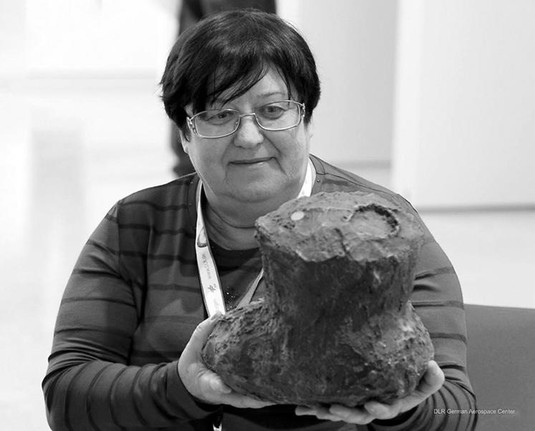 A black-and-white picture of a woman wearing glasses and holding a large model of a dark comet.