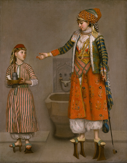 In this painting by Jean Etienne Liotard, a sumptuously clothed woman, wearing the layered garments typical of Ottoman Turkish women’s dress, gestures to her more modestly attired attendant. Every detail of clothing is carefully and accurately rendered in thin, smooth layers of paint, from the sheen of the servant’s striped silk habit to the details of her mistress’s embroidered red robe, loose trousers, and scarves, and the reflected light on her gold coin necklace, filigree bracelet, and delicate rings. The basin (kurna) in the background indicates that the women are in the public bath (hamam), as do the high pattens or clogs (nalin) that both wear to protect their feet from the damp floor. The double-sided comb and pot of henna on the servant’s tray additionally reference the rituals of the bath.