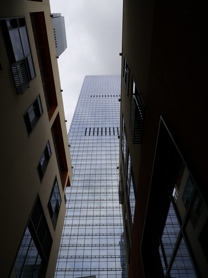 A tall building covered in glass reaches to the sky between two shorter brown buildings