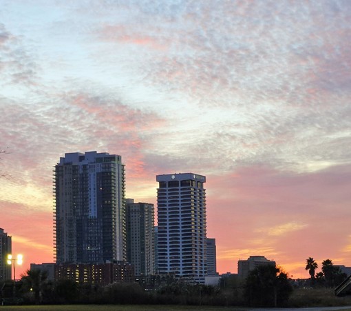 Layes of colors fill the evening sky at sunset with part of the downtown skyline in the foreground.