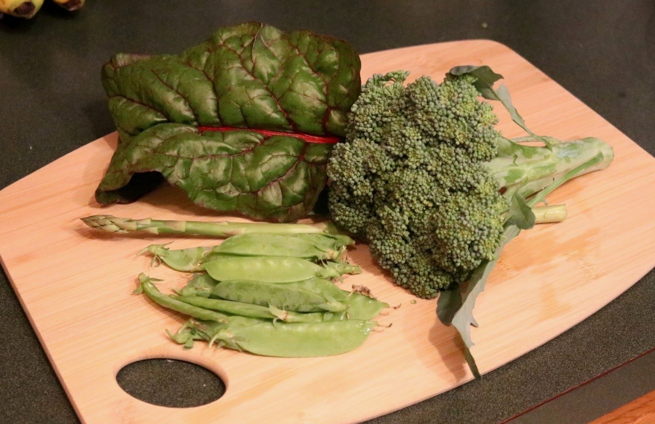 Fresh picked vegetables on a bamboo cutting board. Harvested this evening from my garden. Vegetables include a small head of broccoli (variety "Early Green"), a large Swiss chard leaf (variety "Rhubarb"), a small pile of snow peas (variety "Melting Sugar"), and an asparagus spear.</p><p>Additional notes: the broccoli could have been larger but it was just beginning to show signs of bolting and we're forecast for even warmer weather next week. So I went ahead and picked it. Even though it's small, I'll still get several meals from this one head.