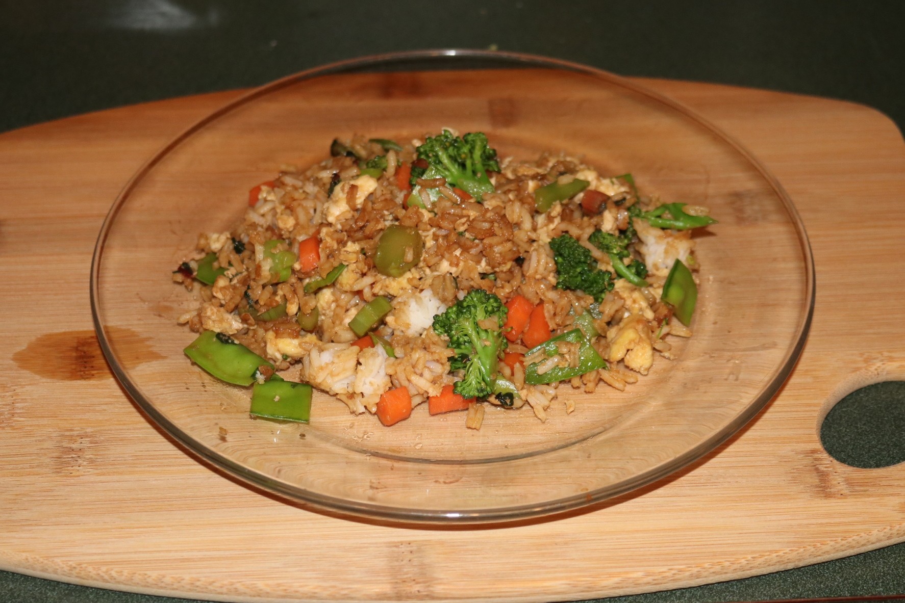 A plate of fried rice on a bamboo cutting board.</p><p>Homegrown vegetables include broccoli, snow peas, swiss chard, asparagus and carrots. Note: the carrots are not shown in first photo because they were pulled up yesterday & already in the fridge. I forgot about them when I took the picture (lol).</p><p>Cooking details: One of my go-to meals that I eat all the time. It's my version of a cross between stir-fry and fried rice. The vegetables are lightly steamed, then cooked along with garlic, ginger, and eggs. Then quickly sautéed over high heat with white rice & soy sauce. Finished with fresh calamondin juice (also grown in my garden) squeezed over the top.
