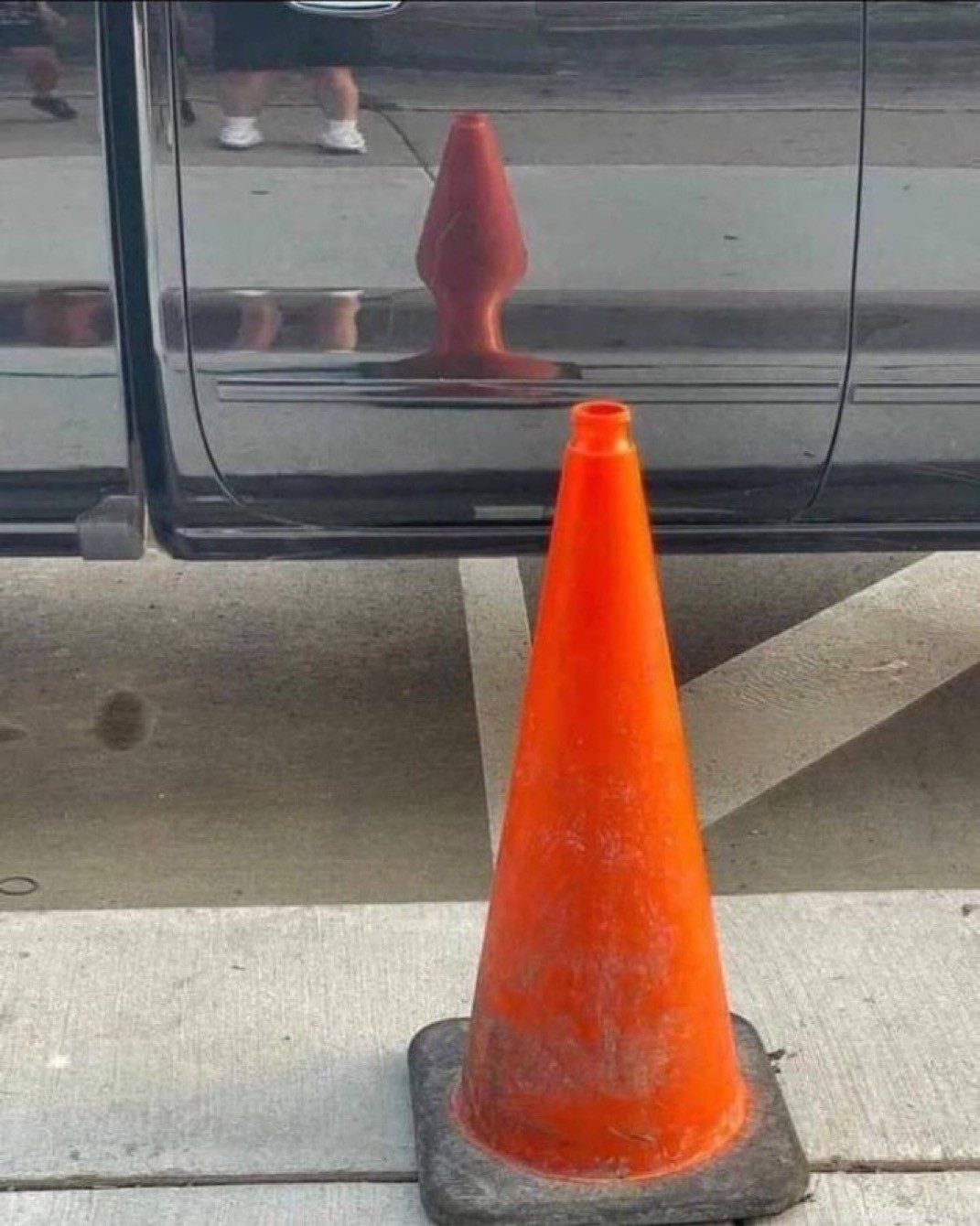 An orange traffic cone’s skewed reflection in a car door closely resembles a butt plug.