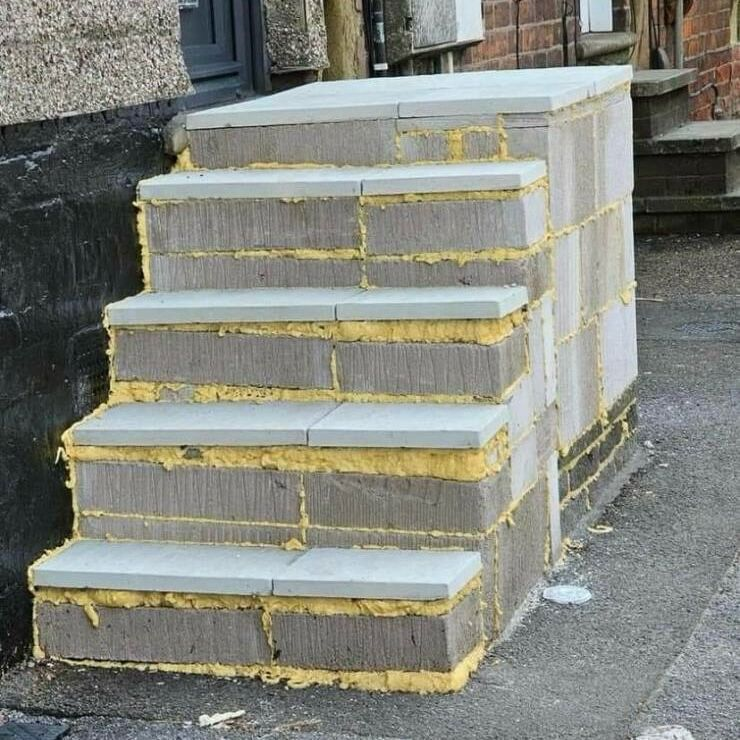 A set of outdoor concrete steps with visible yellow foam insulation between the blocks. The steps lead up to the entrance of a building. A set of outdoor concrete steps with visible yellow foam insulation between the blocks. The steps lead up to the entrance of a building.